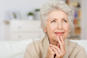 Thoughtful senior lady sitting at home with her fingers to her chin reminiscing and recalling fond memories, close up portrait