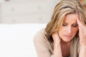 Woman suffering from stress grimacing in pain as she holds the back of her neck with her other hand to her temple, with copyspace